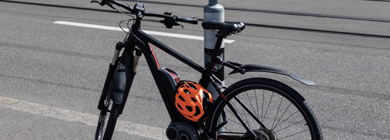 Elektrische fiets met een oranje helm staat tegen een lantaarnpaal aan