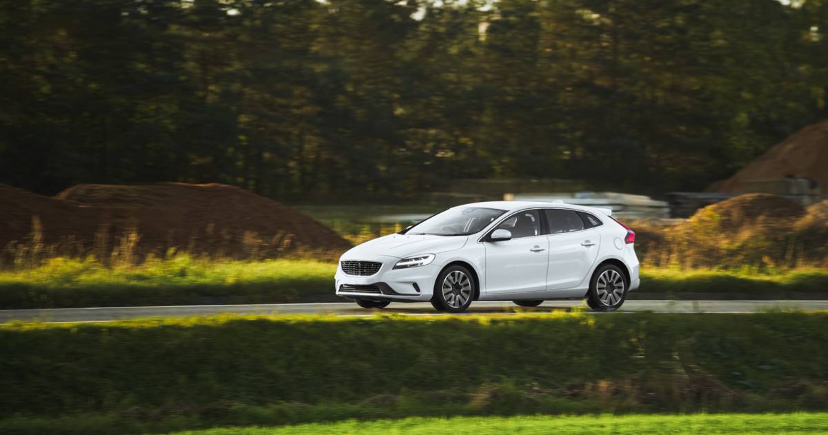 Een witte auto wat aan het rijden is in een beboste omgeving