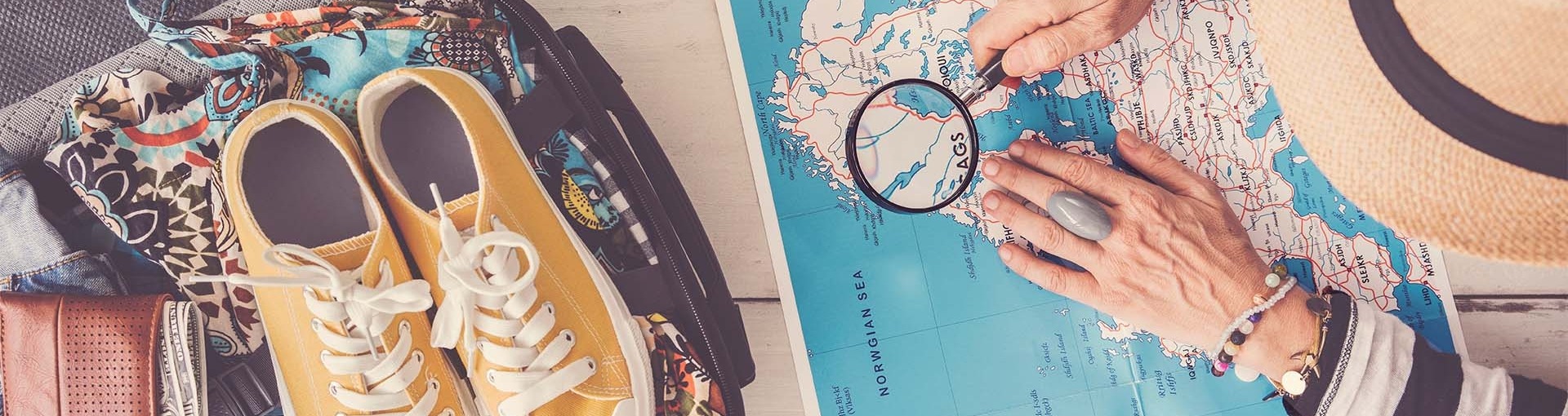 Voorpret vakantie; vrouw bekijkt een landkaart met een loep ernaast stat een ingepakte koffer